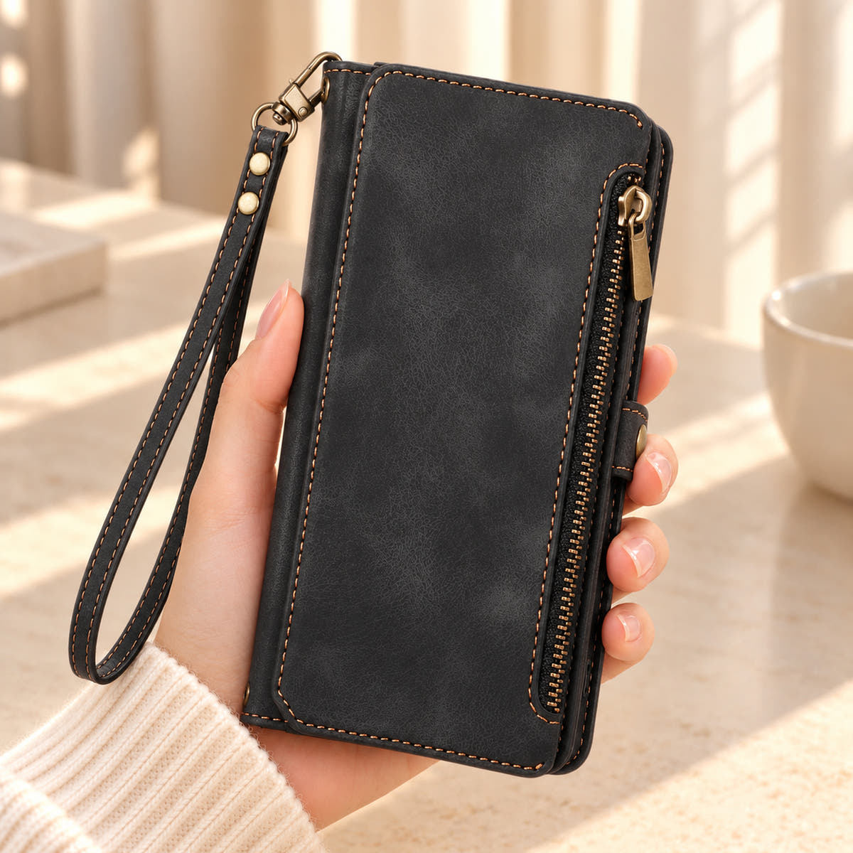 BlushCarry Black wallet phone case held in hand, showing its straight edge zip pocket and matching wrist strap.