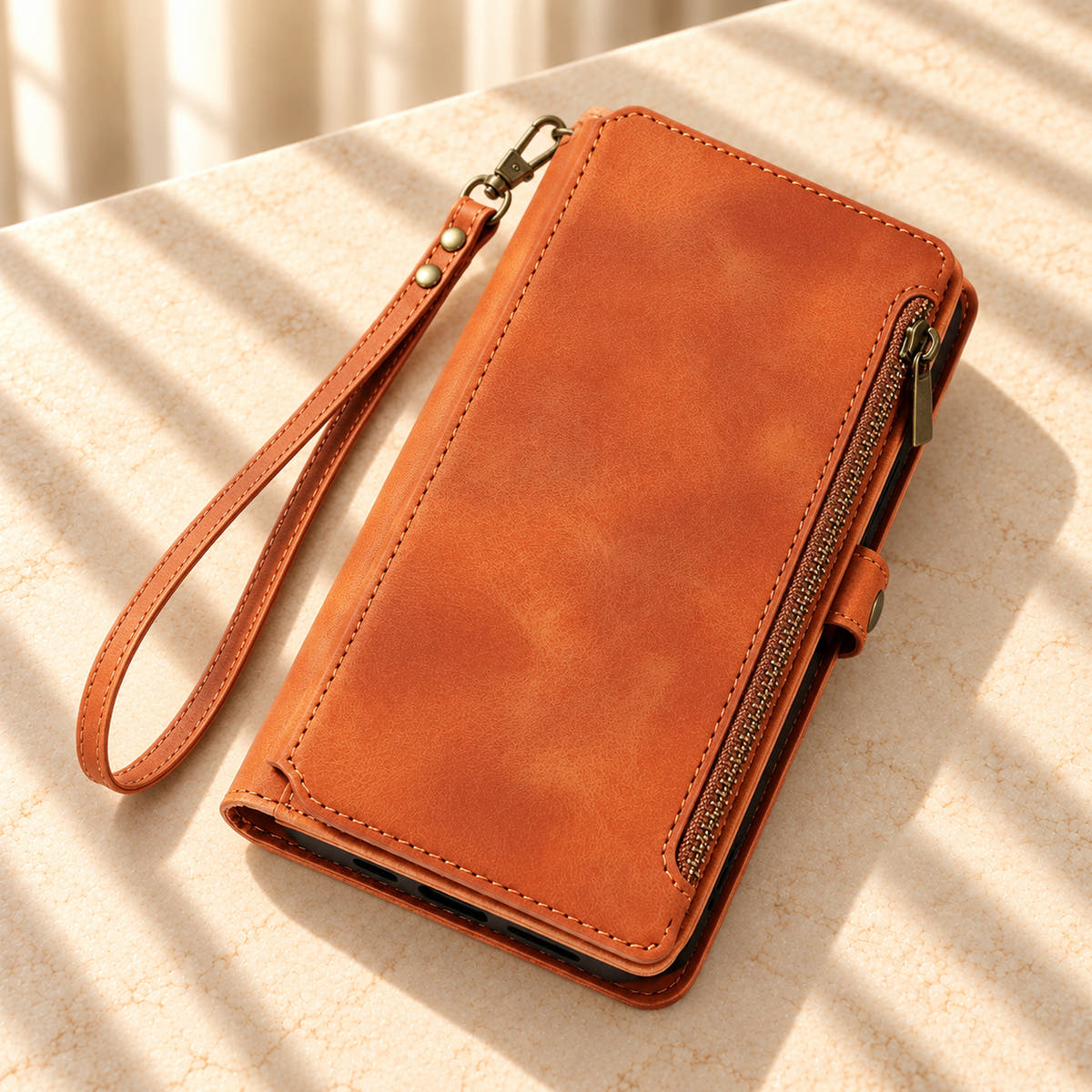 Brown BlushCarry wallet phone case styled diagonally on a sunlit cream tabletop with its edge zip and matching wrist strap.