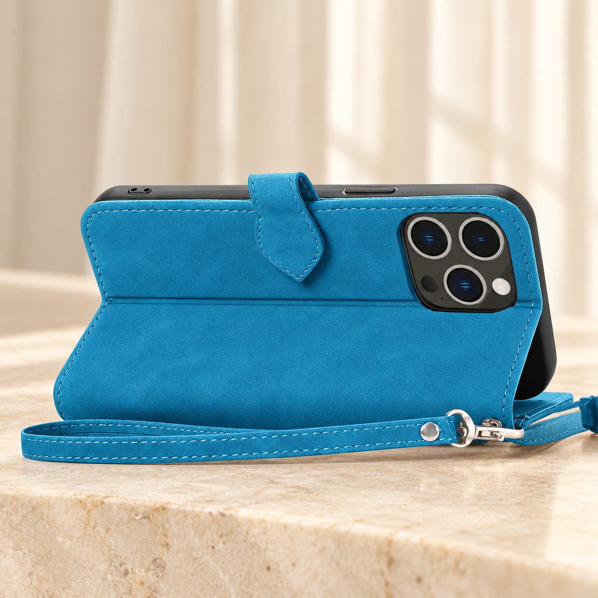 Botanical wallet iPhone case in Blue folded into a landscape stand, rear view showing the plain back, camera opening and matching wrist loop.