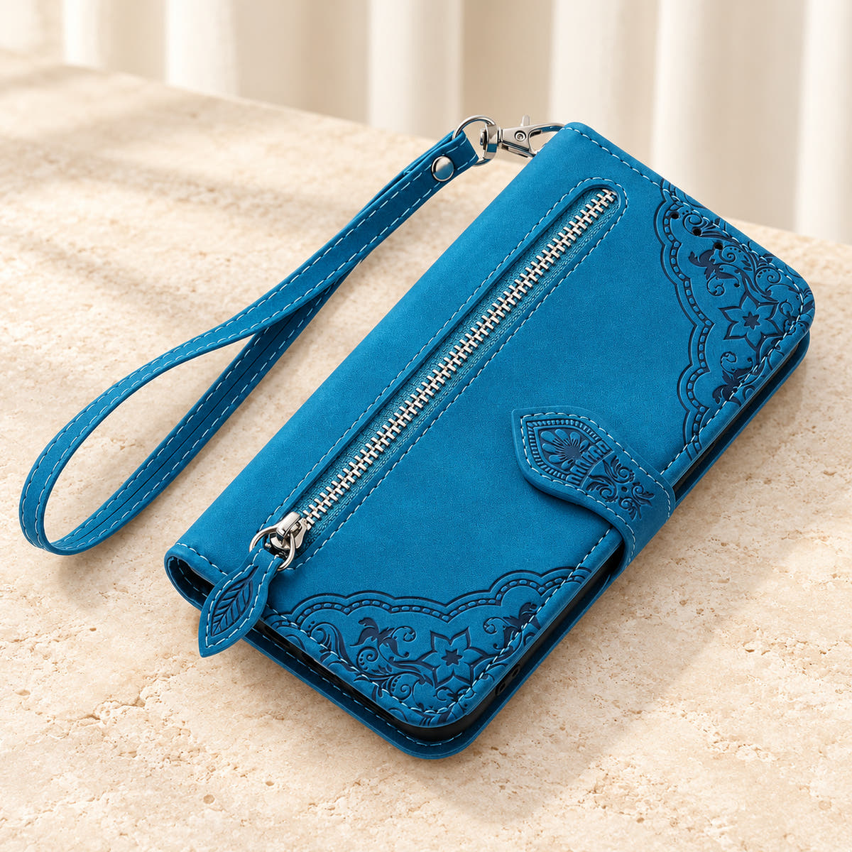 Botanical embossed wallet phone case in Blue, tabletop view of the closed folio with external zip pocket and matching wrist strap.