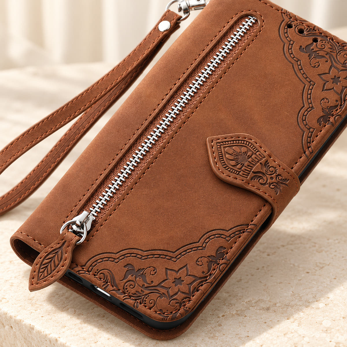 Close-up of the Brown Botanical wallet case showing the silver zipper, leaf-shaped pull, embossed floral border and stitching.