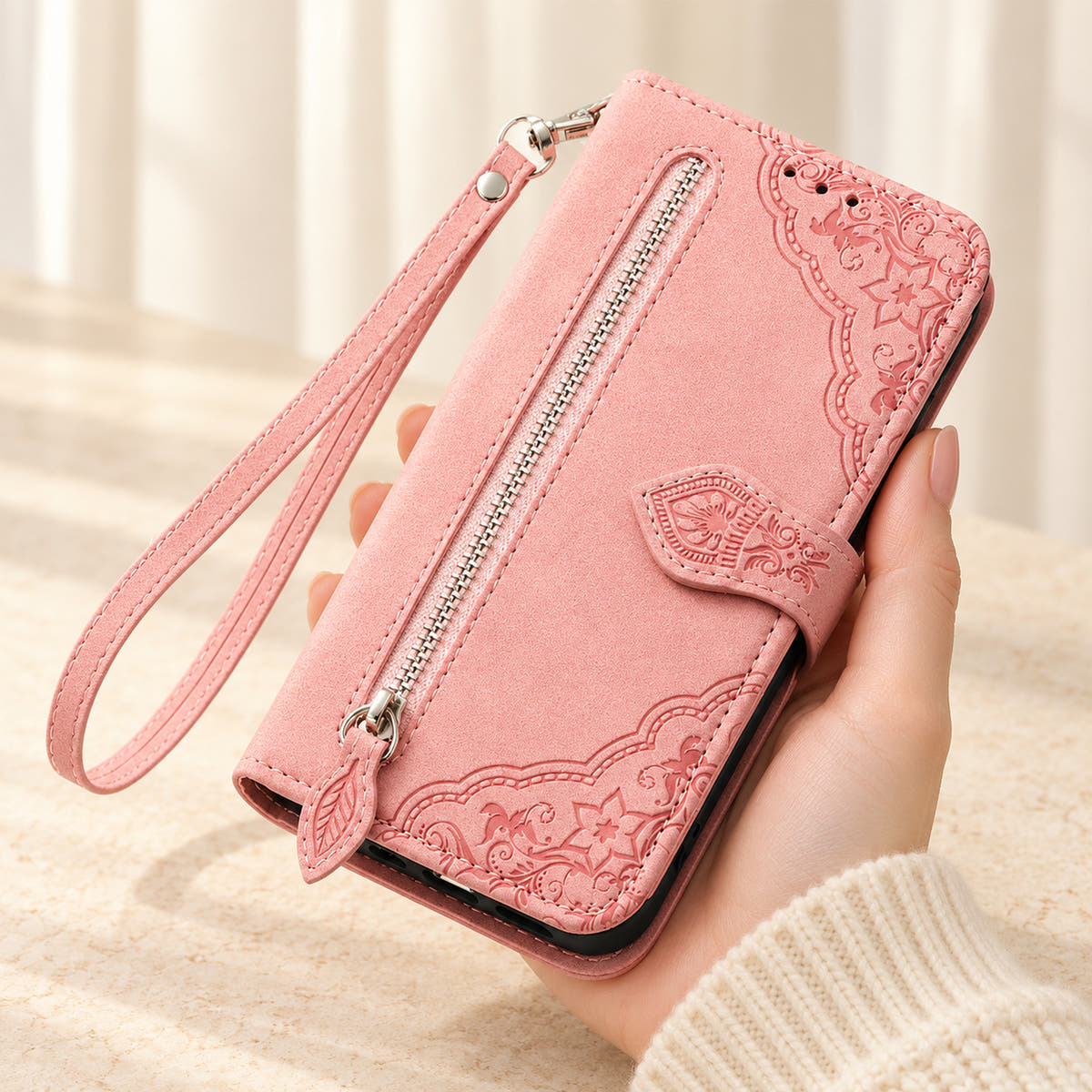 Botanical embossed iPhone wallet case in Pink, handheld front view with silver zip pocket, leaf-shaped pull and matching wrist loop.