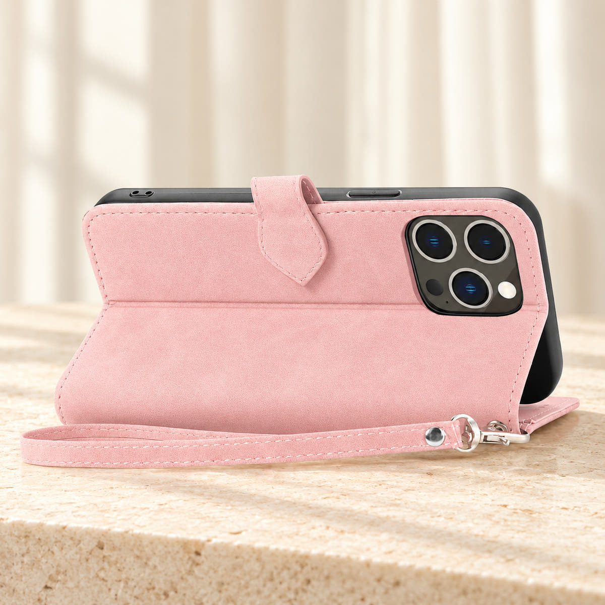 Botanical wallet iPhone case in Pink folded into a landscape stand, rear view showing the plain back, camera opening and matching wrist loop.
