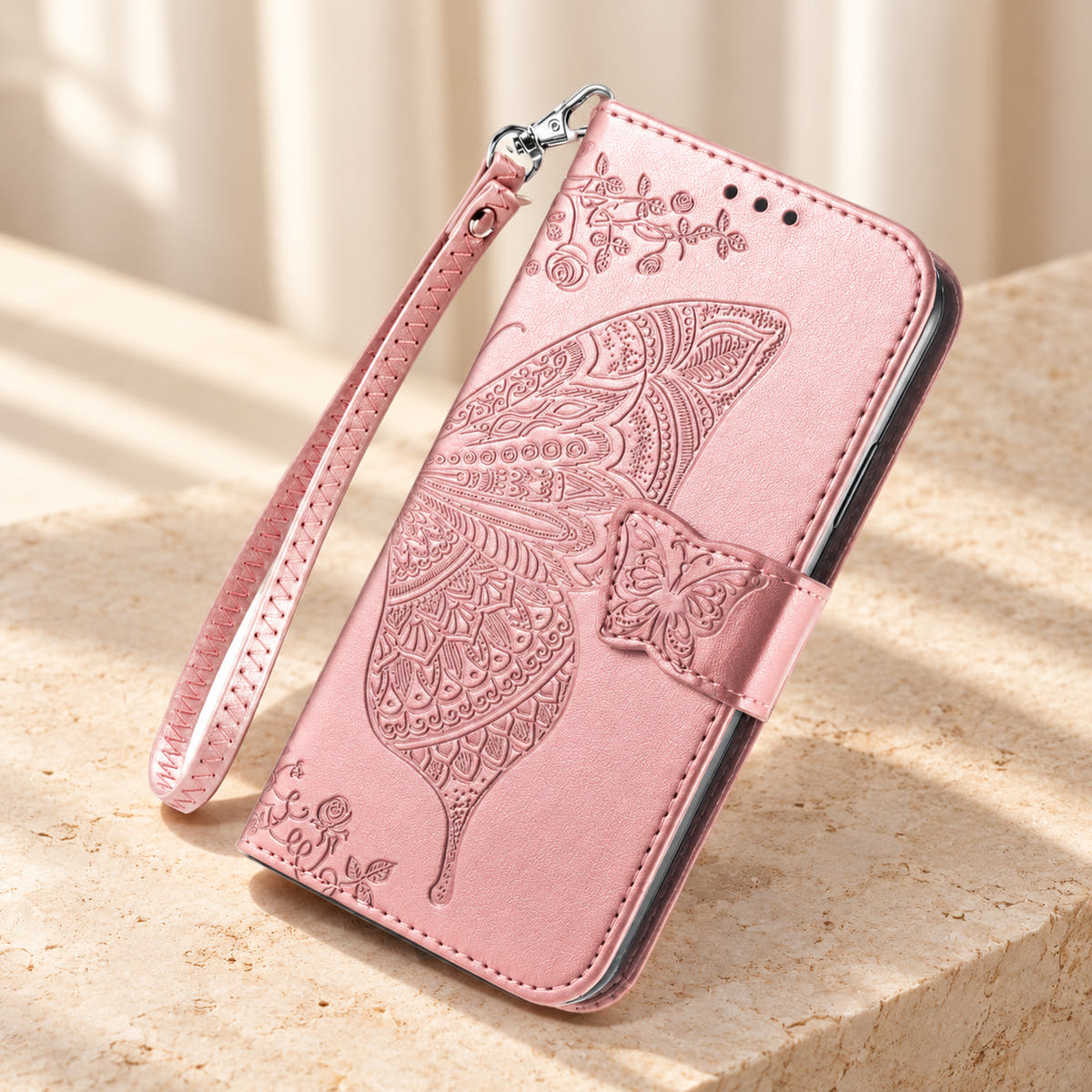Butterfly embossed iPhone wallet case in Baby Pink, tabletop front view showing the detailed wing, tab closure and clip-on wrist loop.
