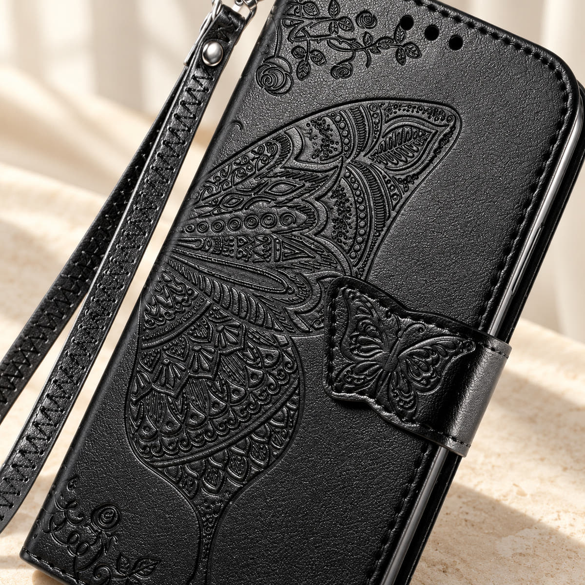 Close-up of the Black Butterfly wallet phone case showing the intricate embossed wing, small butterfly tab and stitched edge.