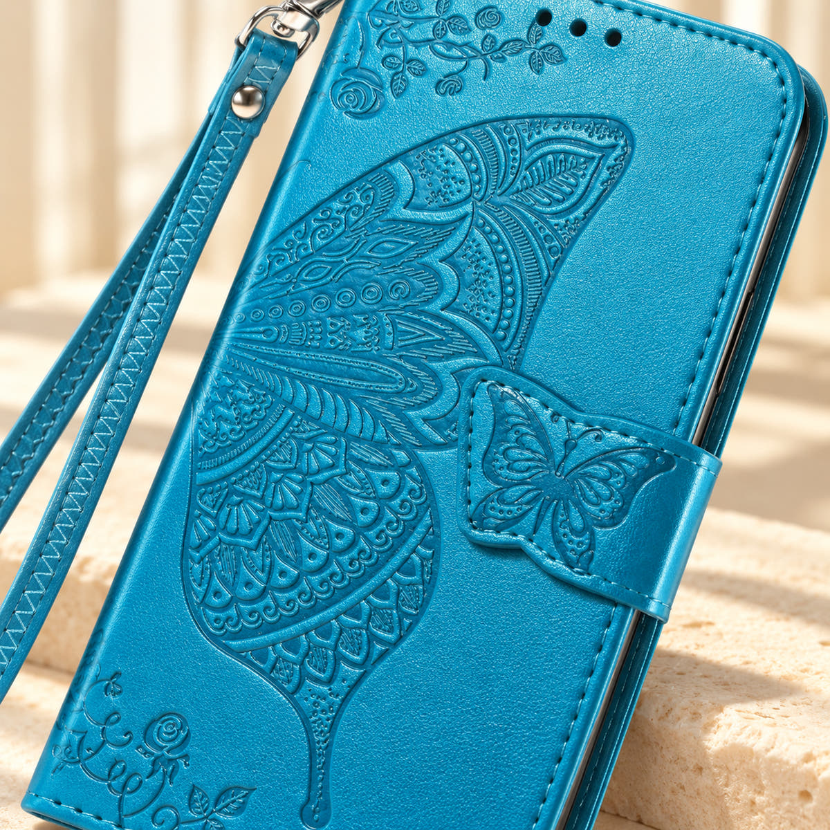 Close-up of the Cloud Blue Butterfly wallet phone case showing the intricate embossed wing, small butterfly tab and stitched edge.