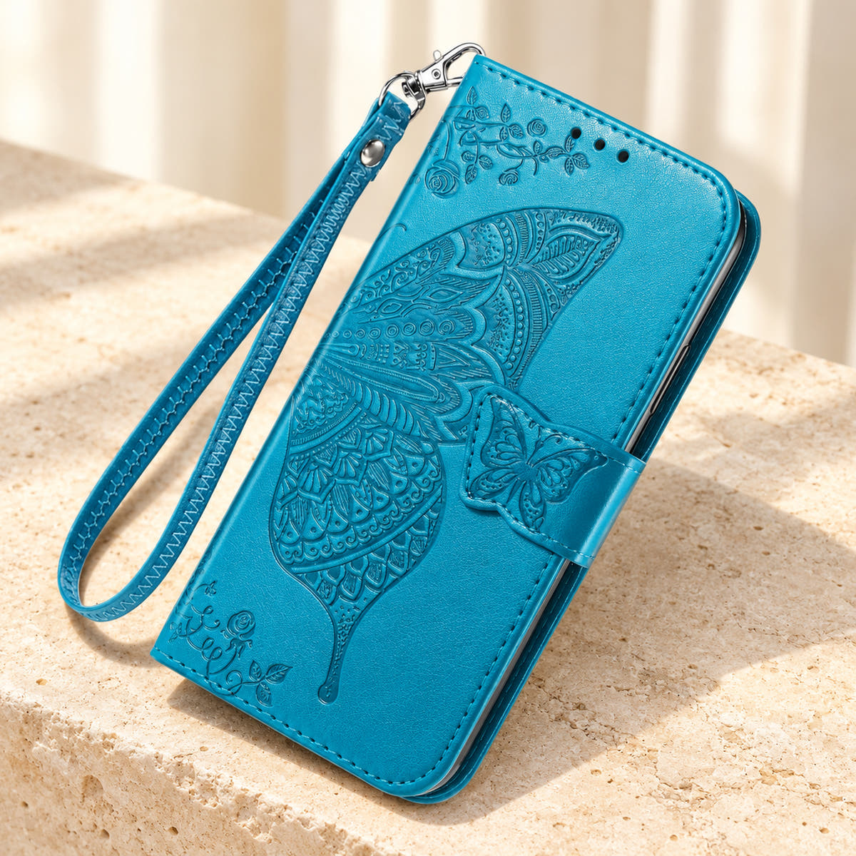 Butterfly embossed iPhone wallet case in Cloud Blue, tabletop front view showing the detailed wing, tab closure and clip-on wrist loop.