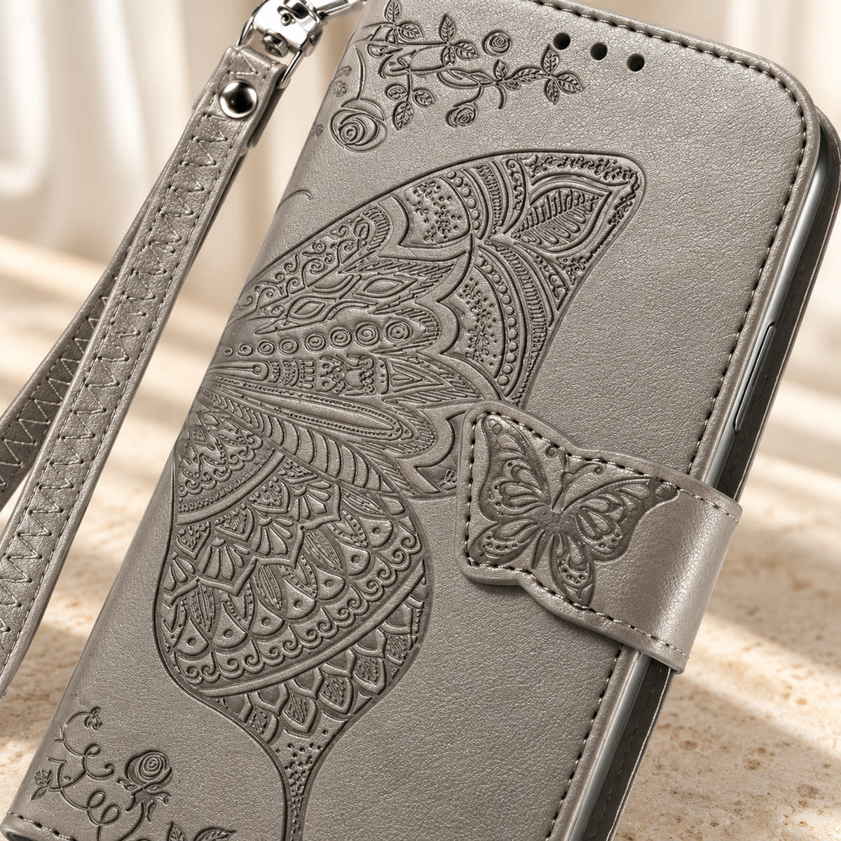 Close-up of the Gray Butterfly wallet phone case showing the intricate embossed wing, small butterfly tab and stitched edge.