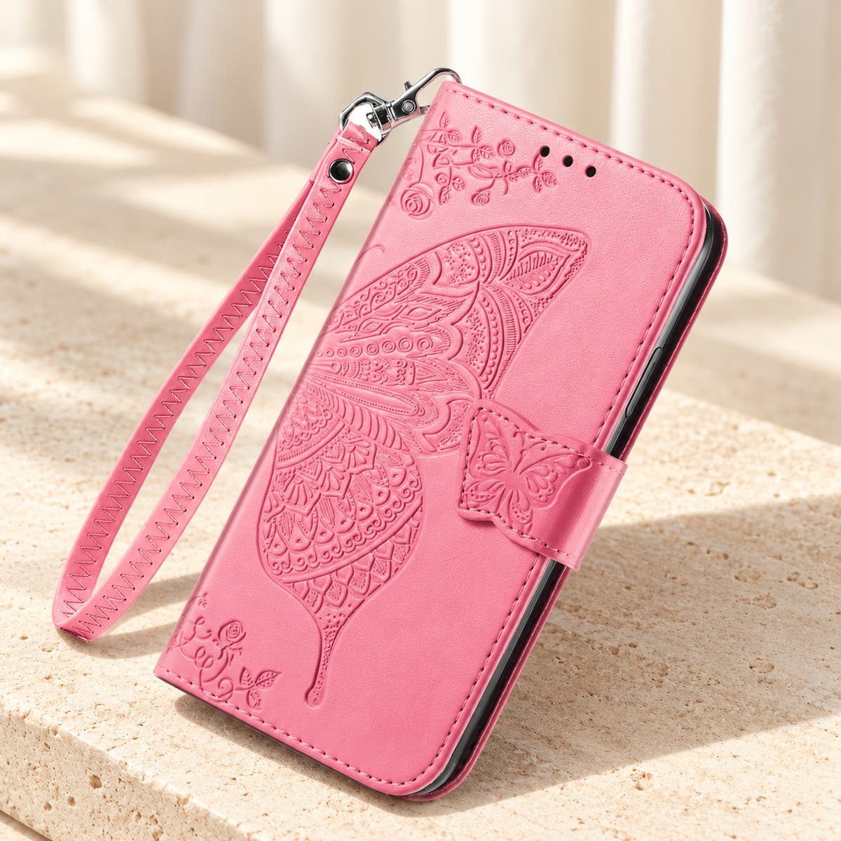 Butterfly embossed iPhone wallet case in Pink, tabletop front view showing the detailed wing, tab closure and clip-on wrist loop.