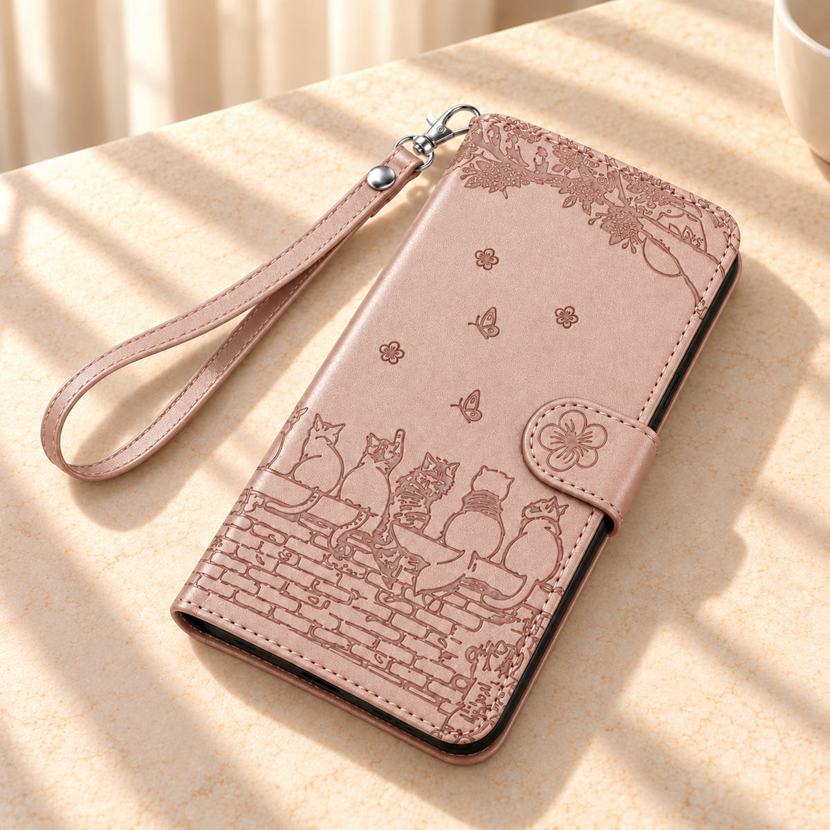 Champagne Pink Cat Garden wallet case and matching wrist strap resting on a cream tabletop.