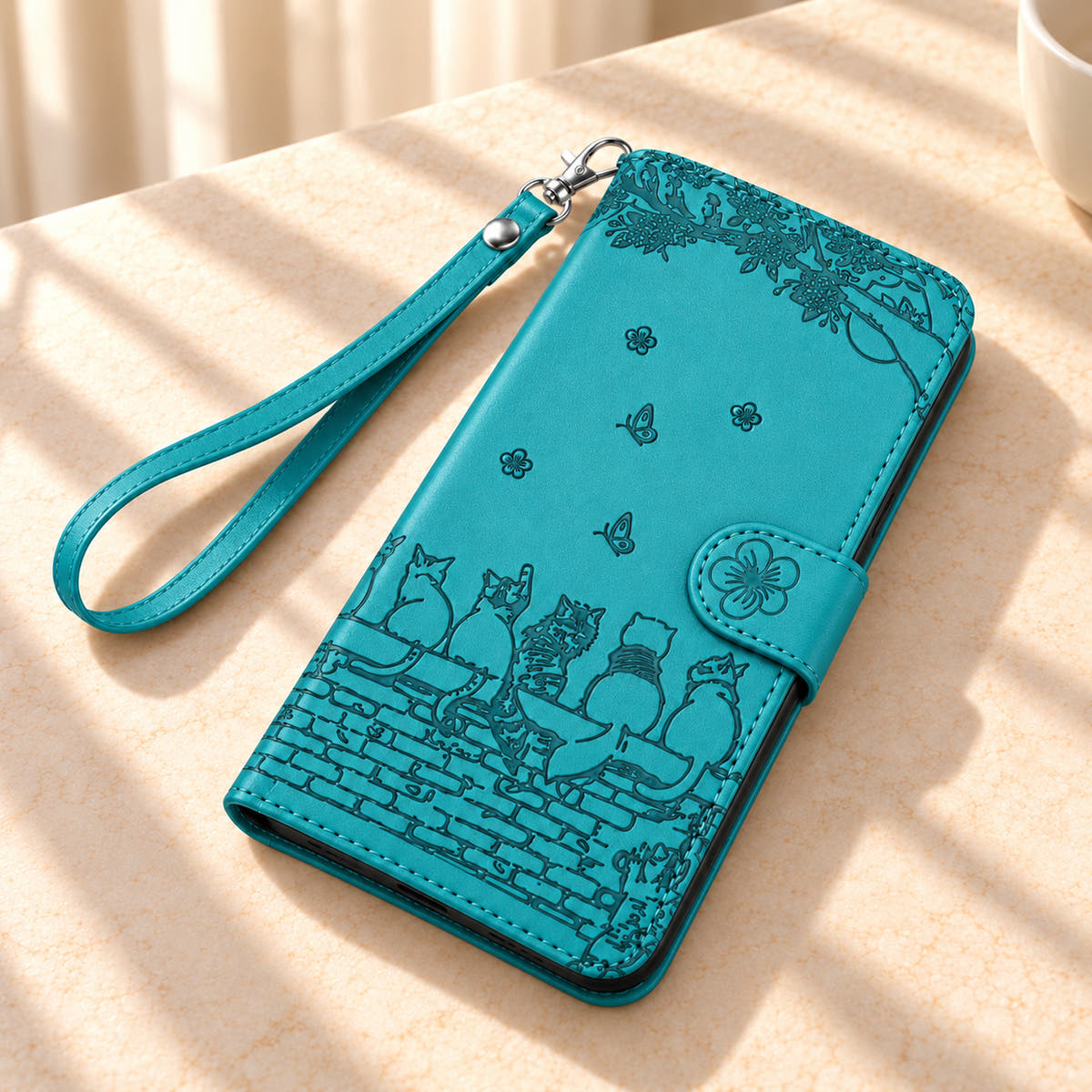 Turquoise Cat Garden wallet case and matching wrist strap on a cream tabletop, with the flower tab closed.