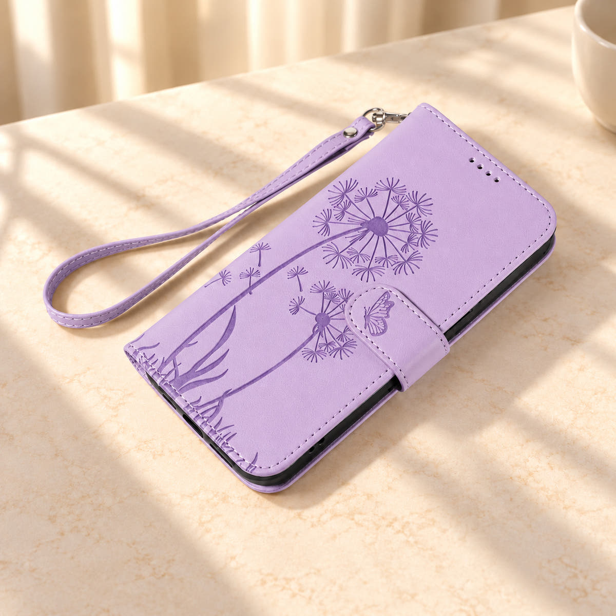 Lavender dandelion wallet phone case lying closed on cream stone beside its matching wrist strap.