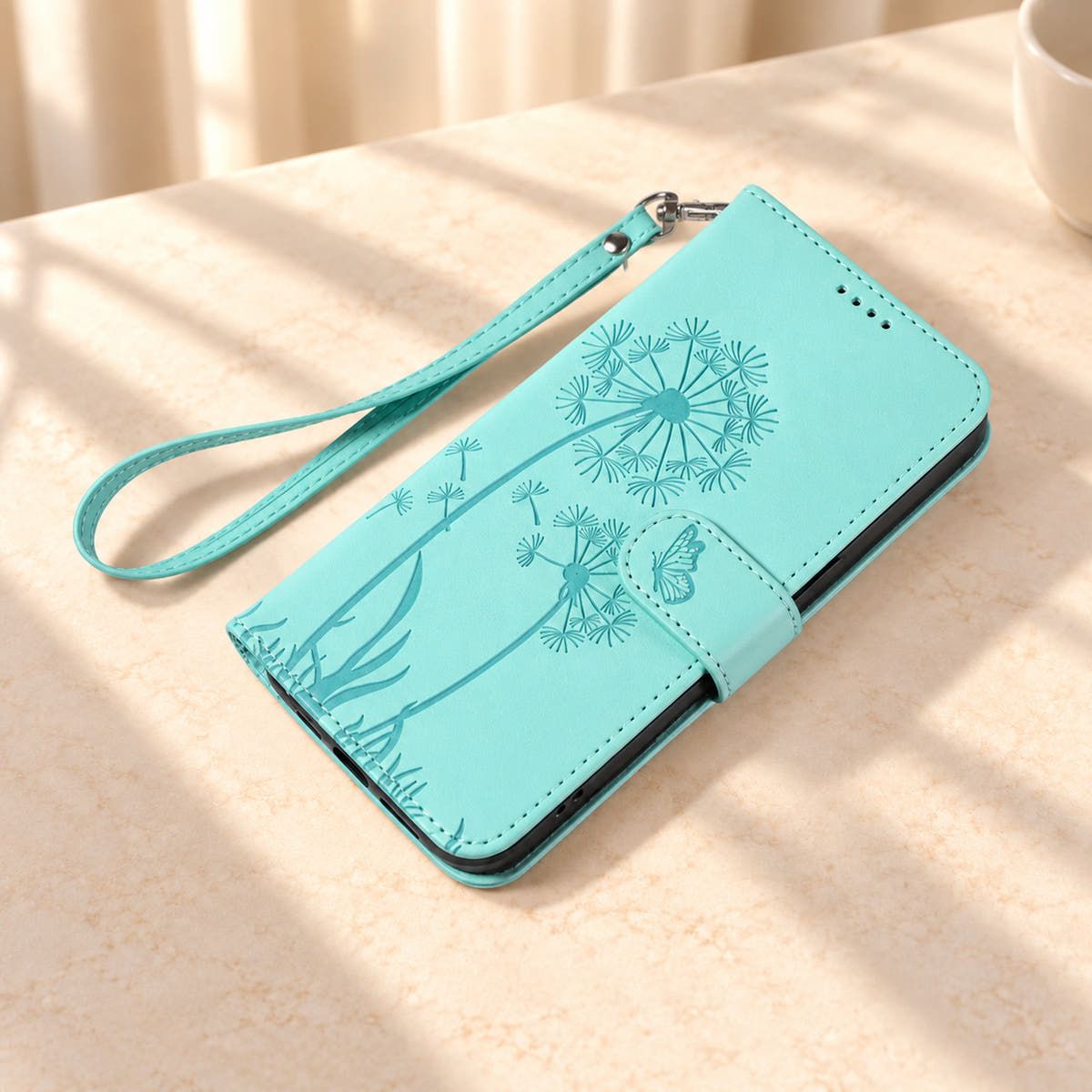 Mint dandelion wallet phone case lying closed on cream stone with its matching wrist strap.