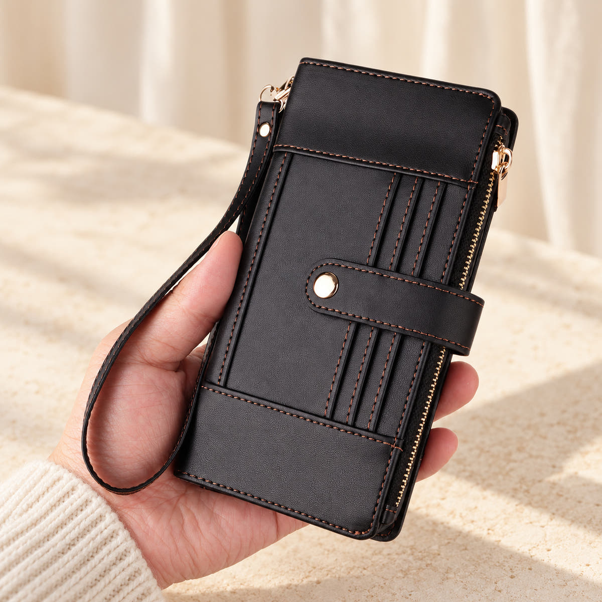 Elaris Crossbody iPhone wallet case in Black, closed handheld view with wrist loop.