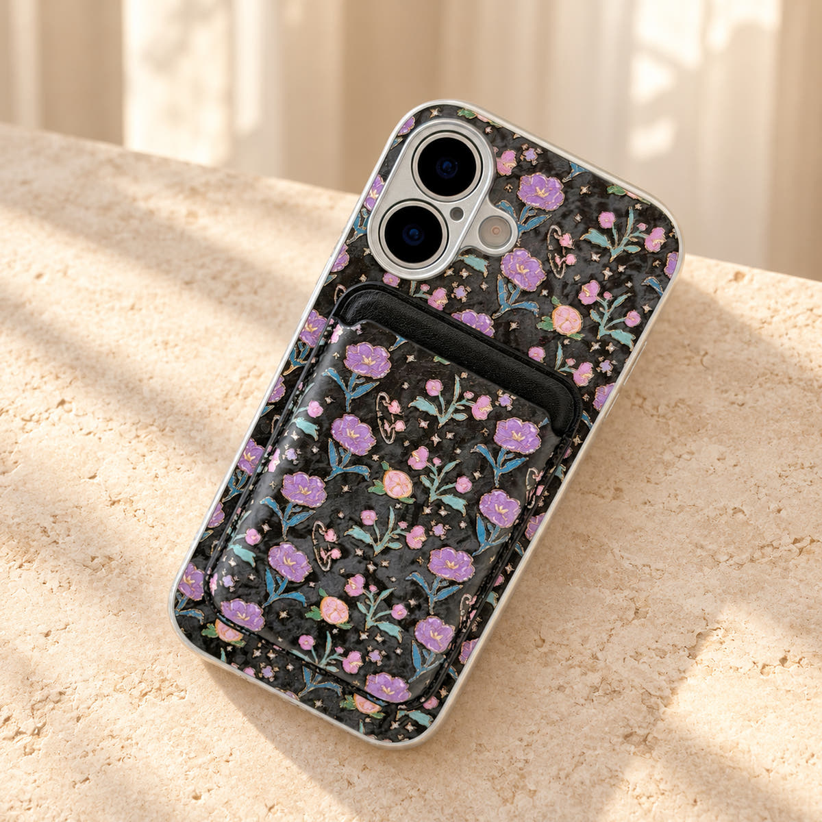 Black Elysia Floral phone case and attached card wallet resting on a warm cream stone tabletop.
