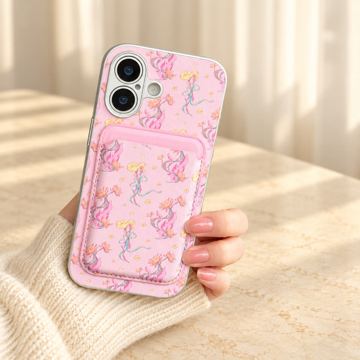 Pink Elysia Floral iPhone case held in a cream-sleeved hand with its matching card wallet attached.