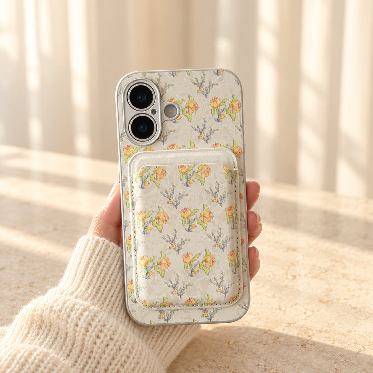 Yellow Elysia Floral iPhone case held in a cream-sleeved hand with its matching card wallet attached.