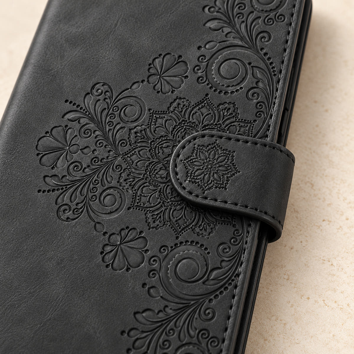 Floral embossed iPhone flip wallet case in Black — close-up of floral embossing, closure tab and stitching