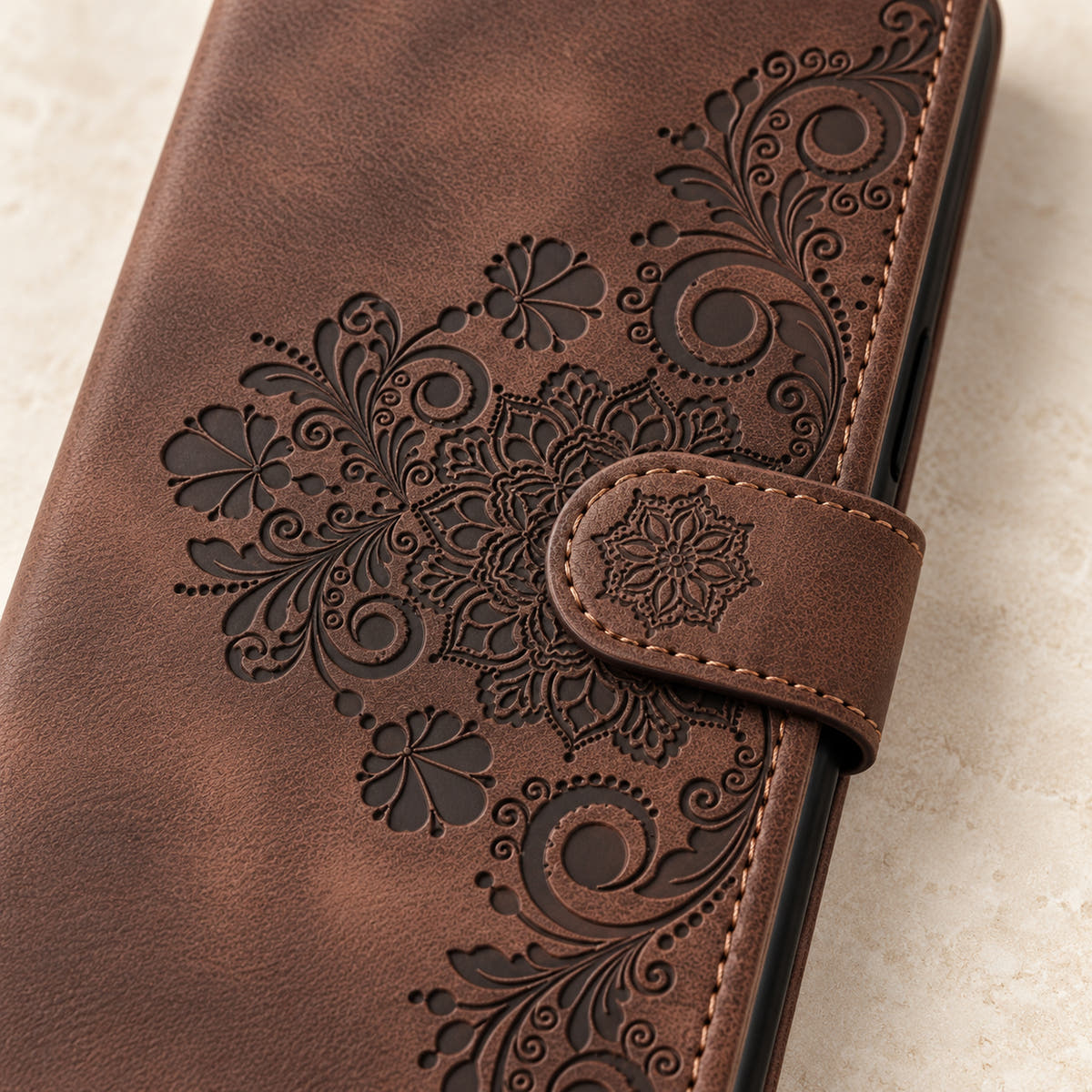 Floral embossed iPhone flip wallet case in Brown — close-up of floral embossing, closure tab and stitching