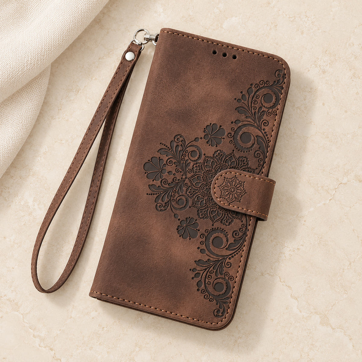 Floral embossed iPhone flip wallet case in Brown — overhead view of floral front and matching wrist strap
