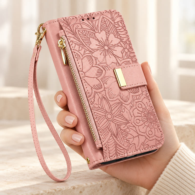 Pink floral iPhone wallet case held in hand, showing embossed flowers, gold-tone closure, front zip pouch and matching wrist strap