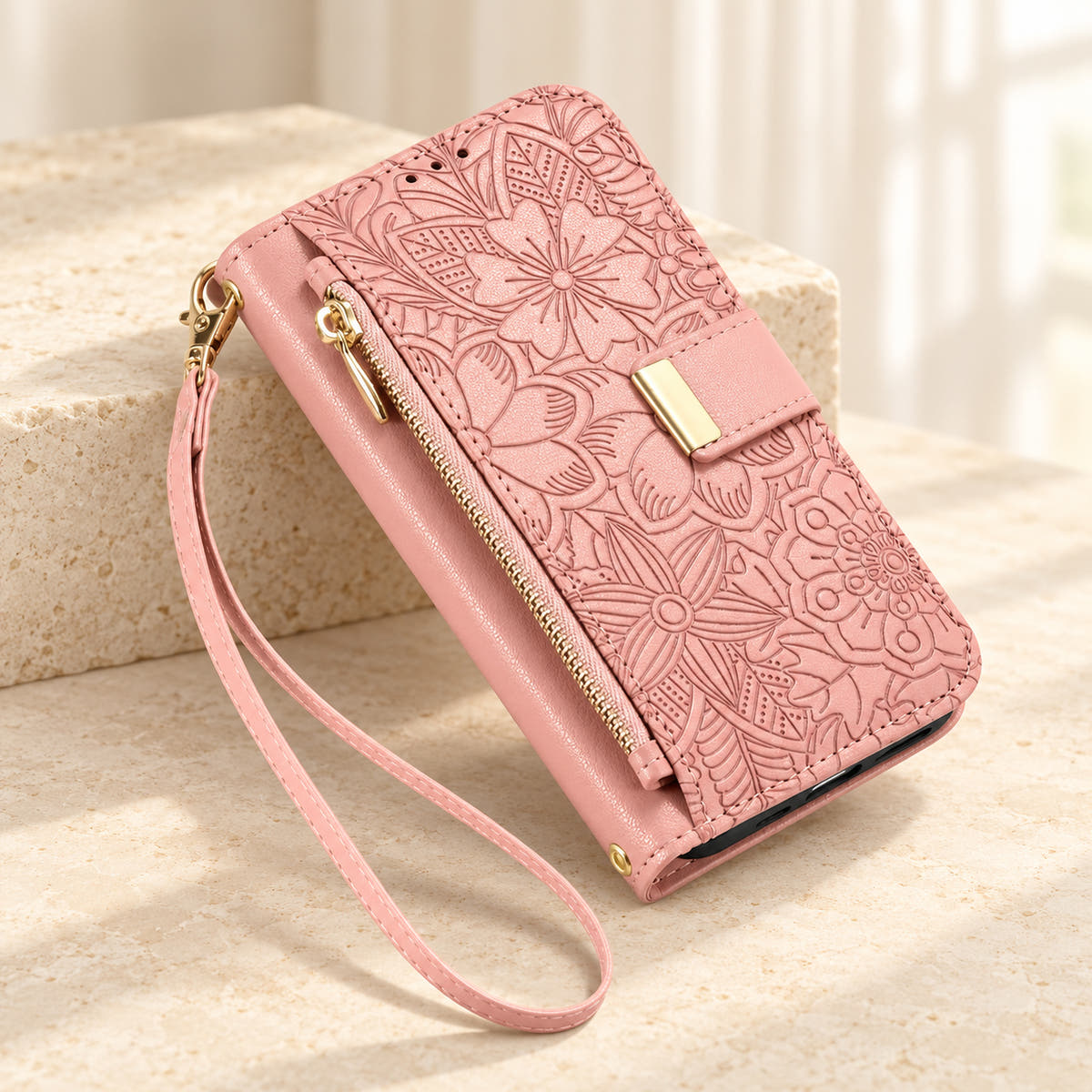 Pink embossed floral iPhone wallet case on a cream surface with the closed zip pouch, gold-tone tab and matching wrist loop
