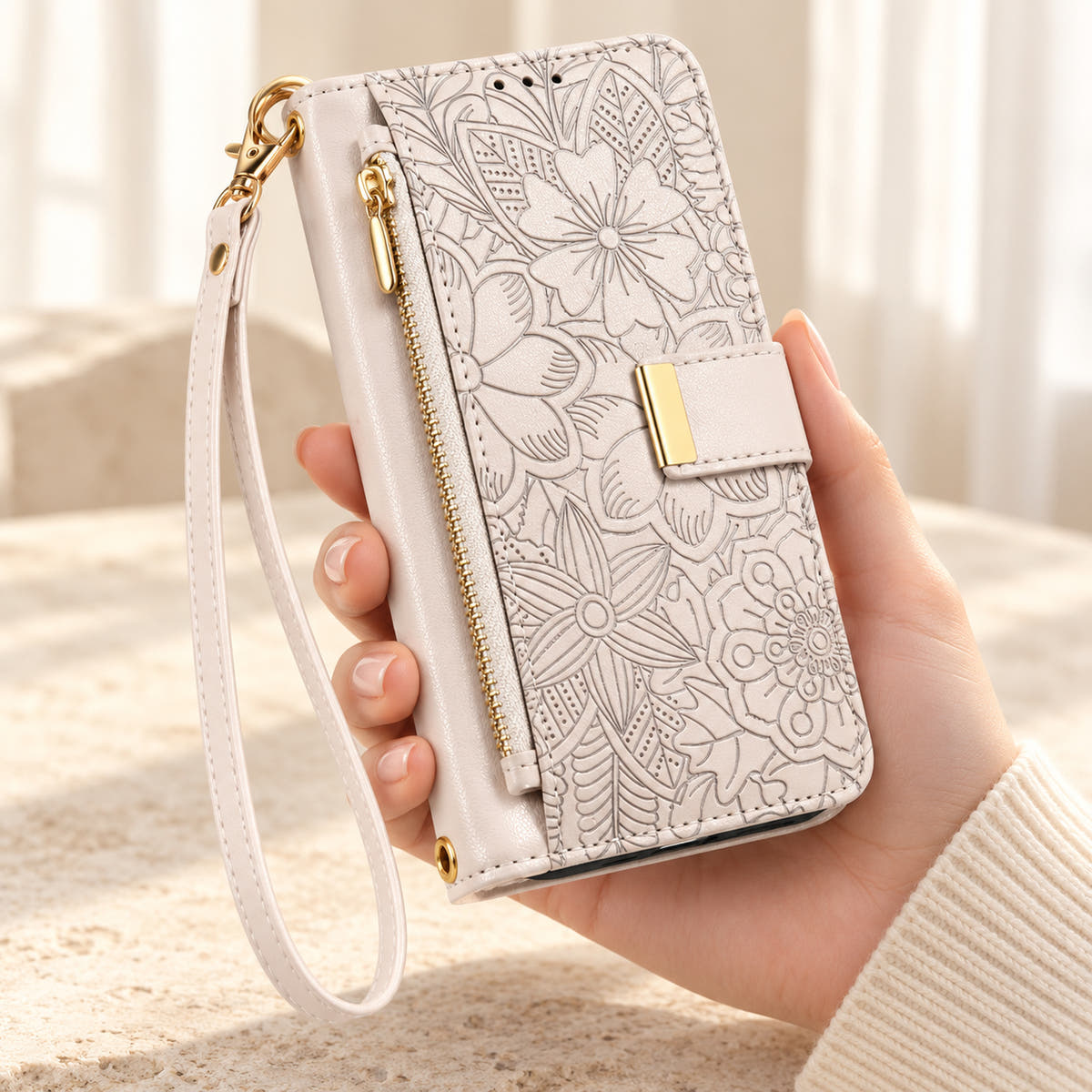 White floral iPhone wallet case held in hand, showing embossed flowers, gold-tone closure, front zip pouch and matching wrist strap
