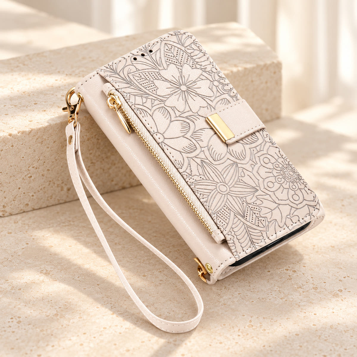 White embossed floral iPhone wallet case on a cream surface with the closed zip pouch, gold-tone tab and matching wrist loop