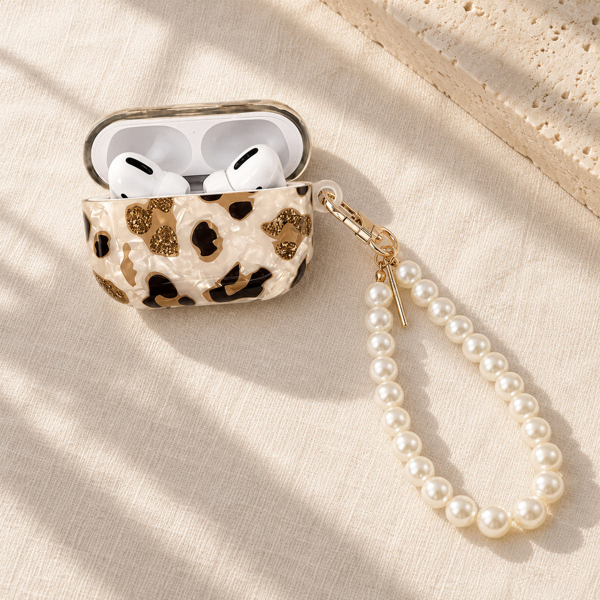 Gilded Leopard Heart AirPods case Design #1 — linen flatlay showing its pearl-style wrist loop