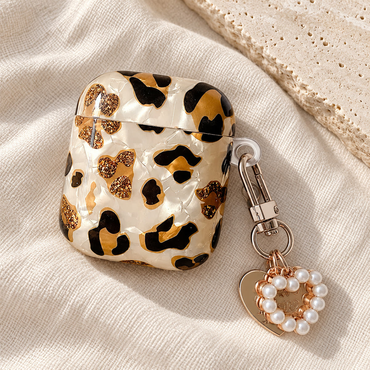 Gilded Leopard Heart AirPods case Design #2 — linen flatlay showing its pearl-style heart charm