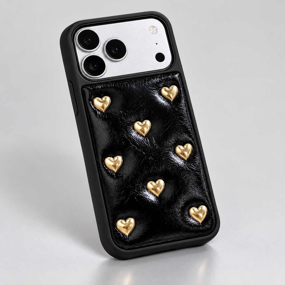 Black iPhone case with raised gold-tone hearts — black texture under side light.