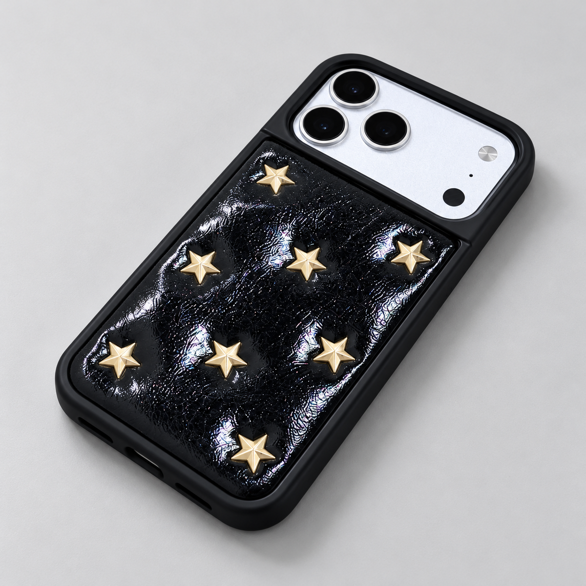 Black iPhone case with raised gold-tone stars — black texture under side light.