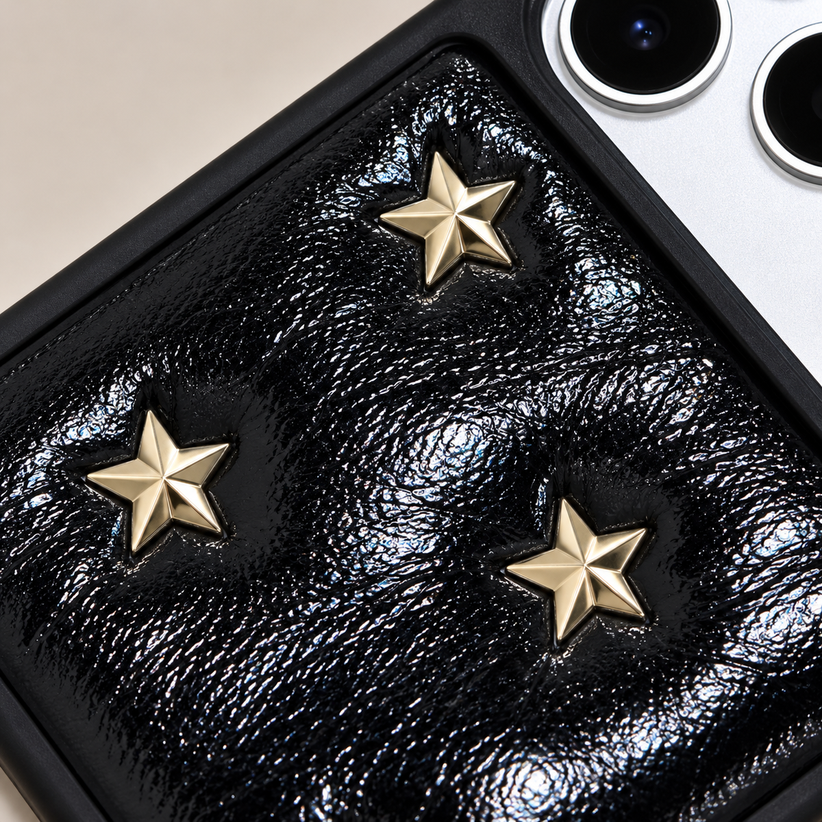 Black iPhone case with raised gold-tone stars — gold-tone motif close-up.