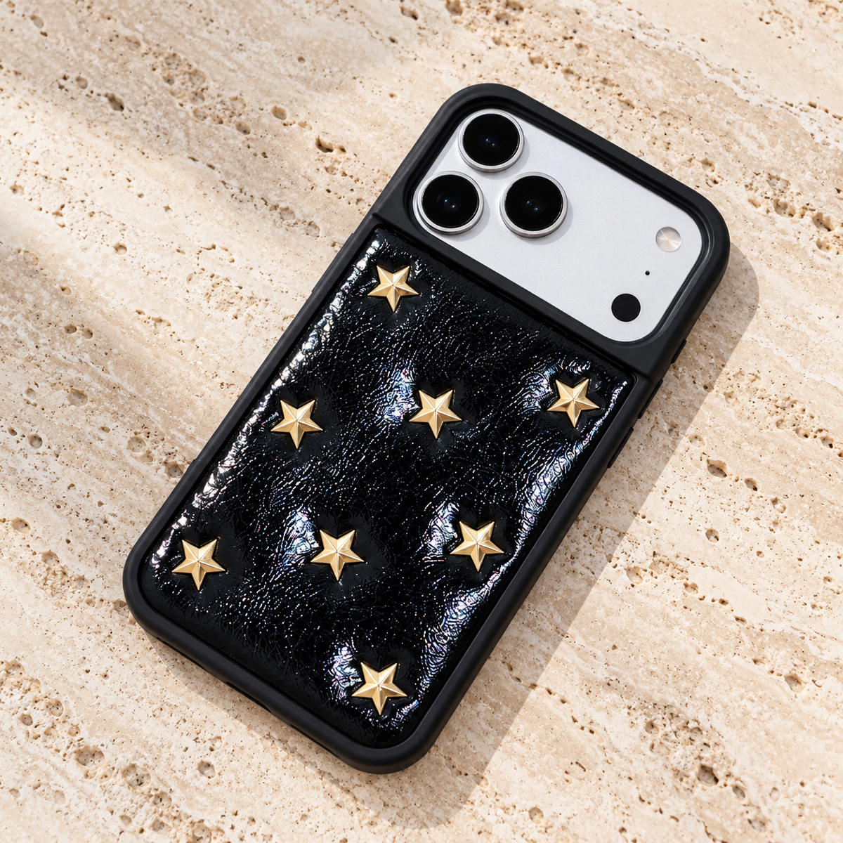 Black iPhone case with raised gold-tone stars — angled tabletop view.