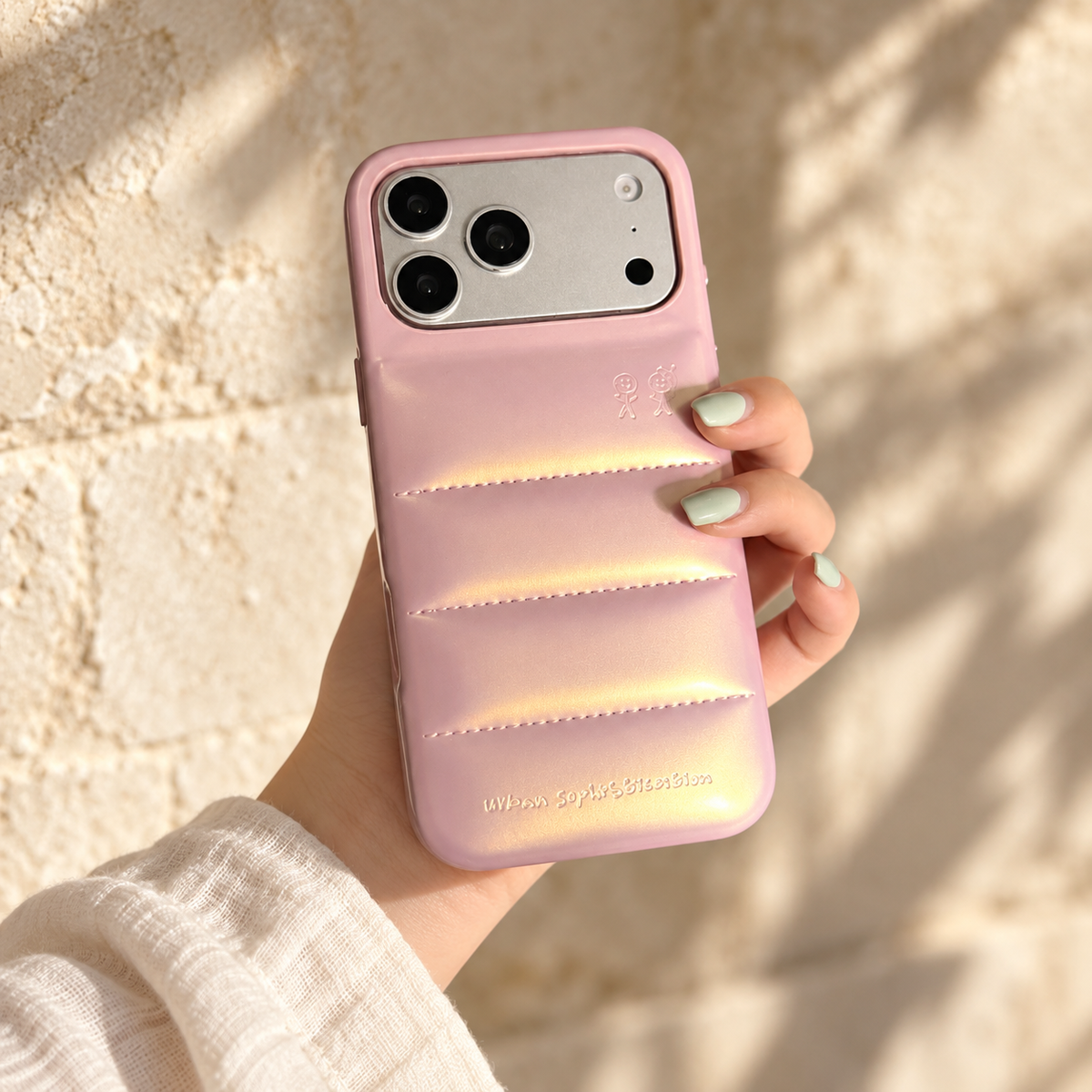 Iridescent Pink puffer iPhone case held upright in a hand against warm cream surroundings.