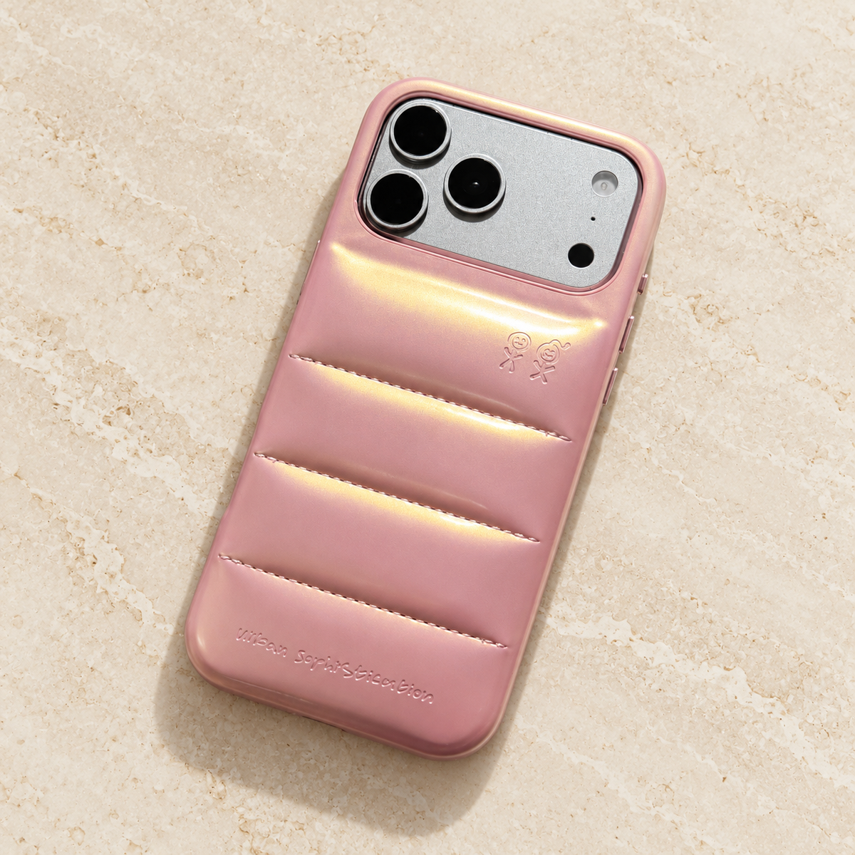 Iridescent Pink puffer iPhone case resting diagonally on a warm limestone tabletop.
