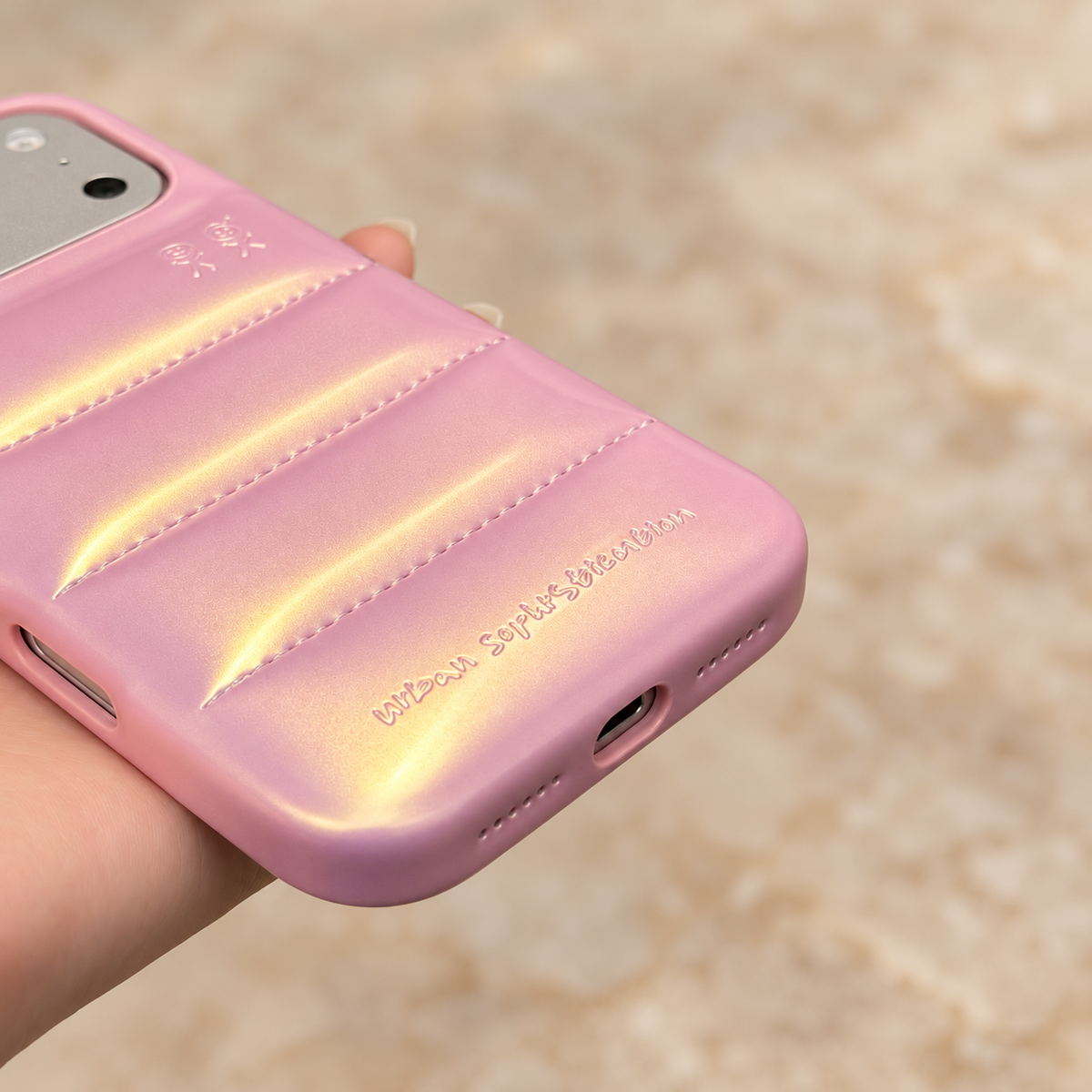 Lower-edge view of the Iridescent Pink puffer phone case showing the charging opening, small perforations and embossed lettering.