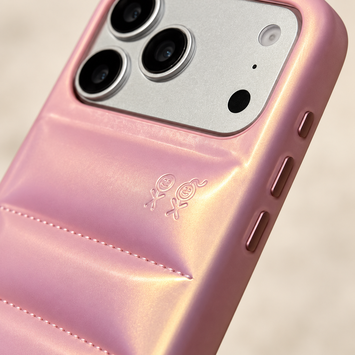 Close-up of the two small embossed figures above a stitched seam on the Iridescent Pink puffer case.