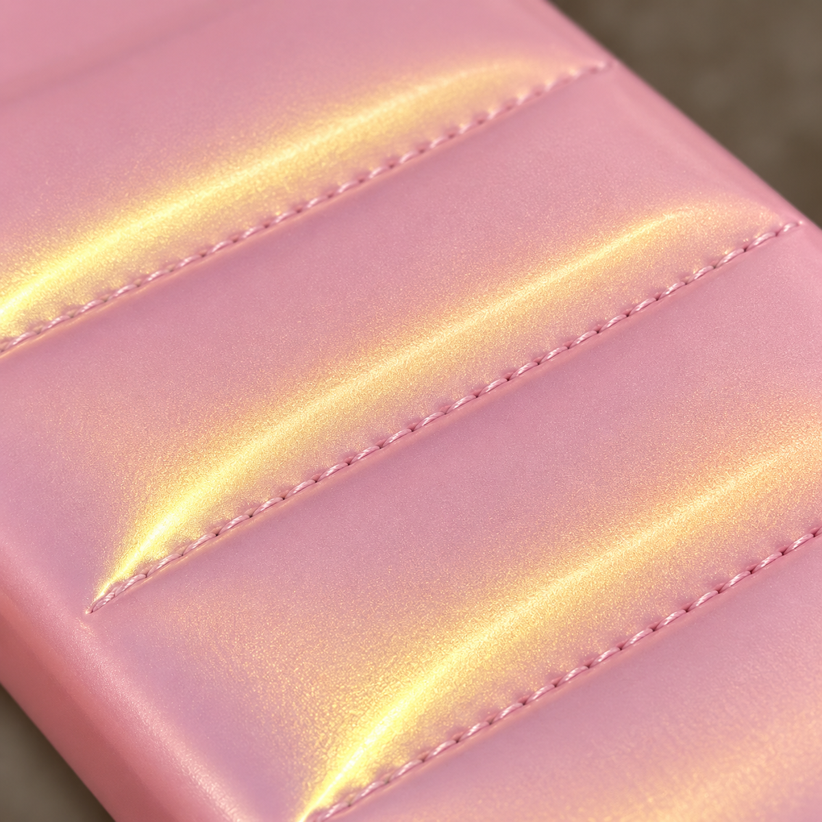 Macro detail of the lower stitched seams and golden highlights on the Iridescent Pink puffer case.