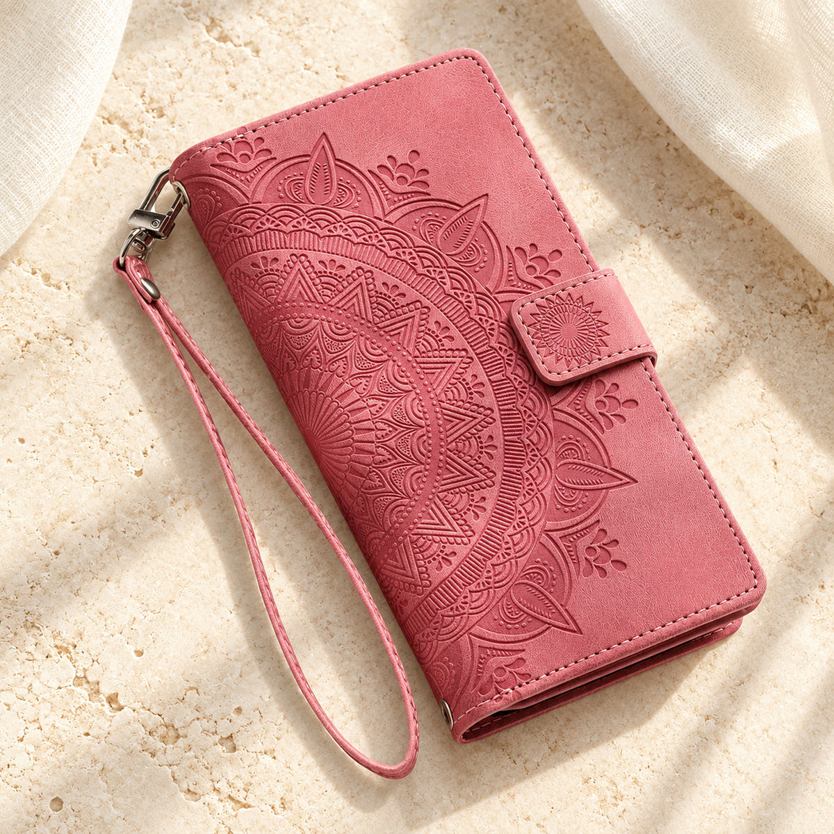 Lotus Mandala iPhone wallet case in Pink showing the closed embossed cover and matching wrist loop on limestone