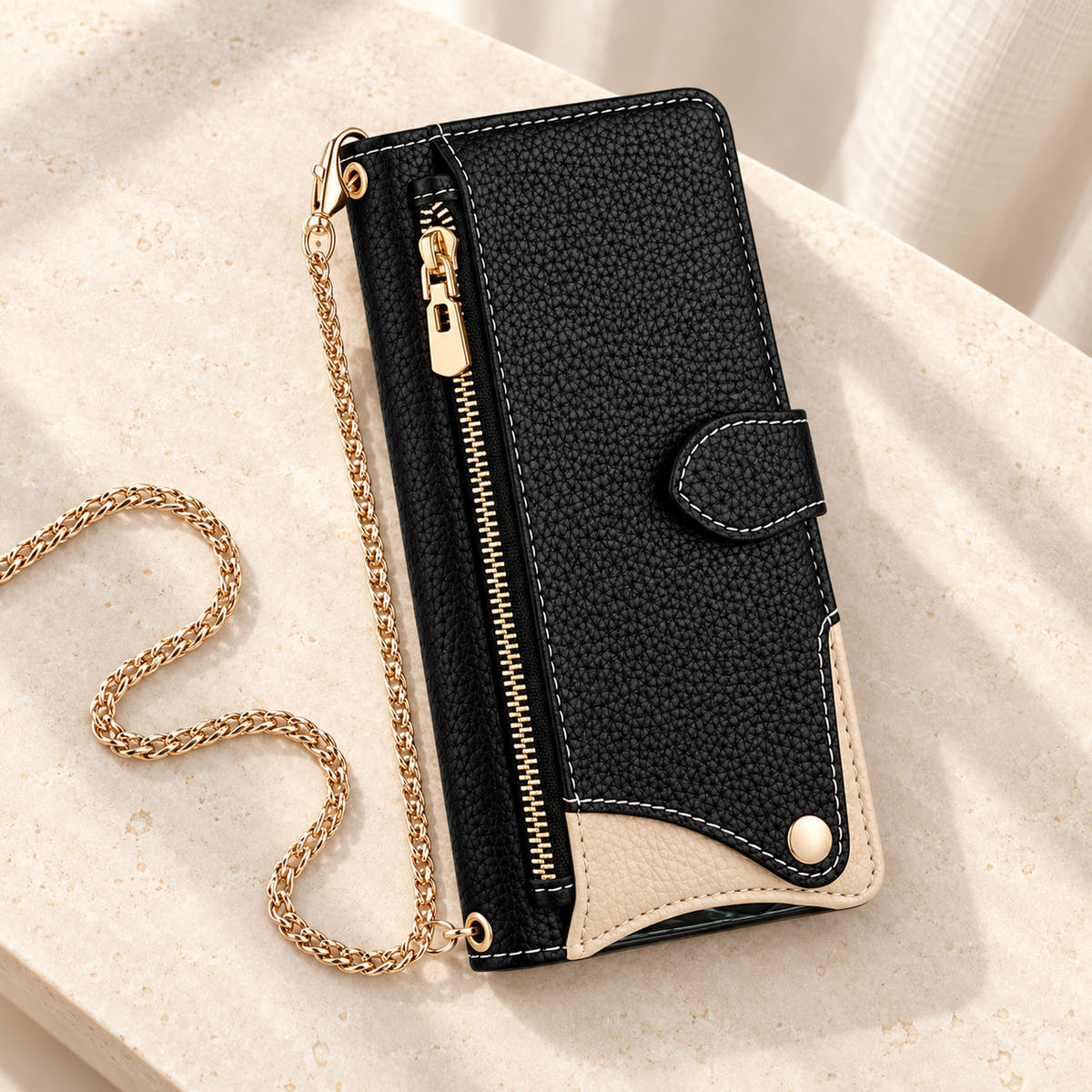 Luxe Colourblock iPhone wallet case in Black with gold-tone chain arranged on cream limestone