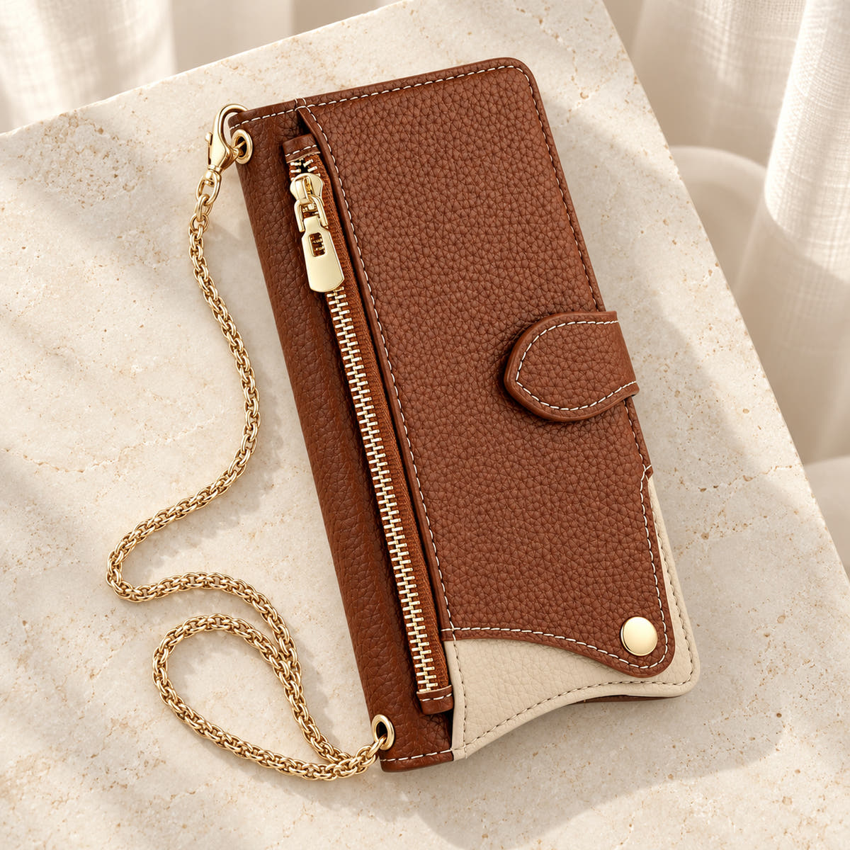 Luxe Colourblock iPhone wallet case in Brown with gold-tone chain arranged on cream limestone