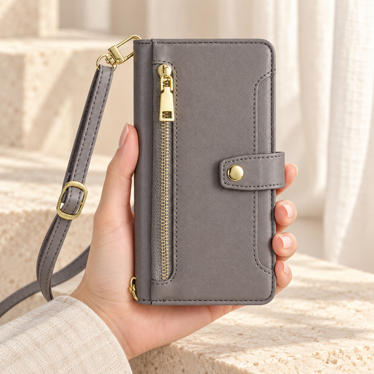 Minimal crossbody iPhone wallet case in Gray — front held in hand showing gold-tone zip and closure tab