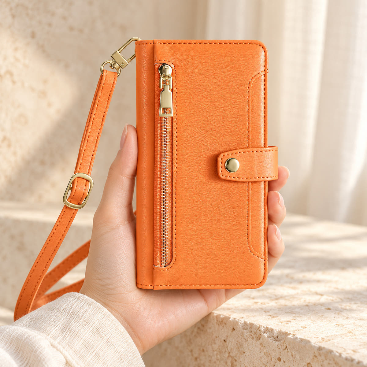 Minimal crossbody iPhone wallet case in Orange — front held in hand showing gold-tone zip and closure tab