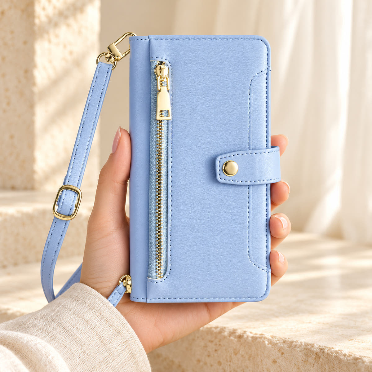 Minimal crossbody iPhone wallet case in Sky Blue — front held in hand showing gold-tone zip and closure tab