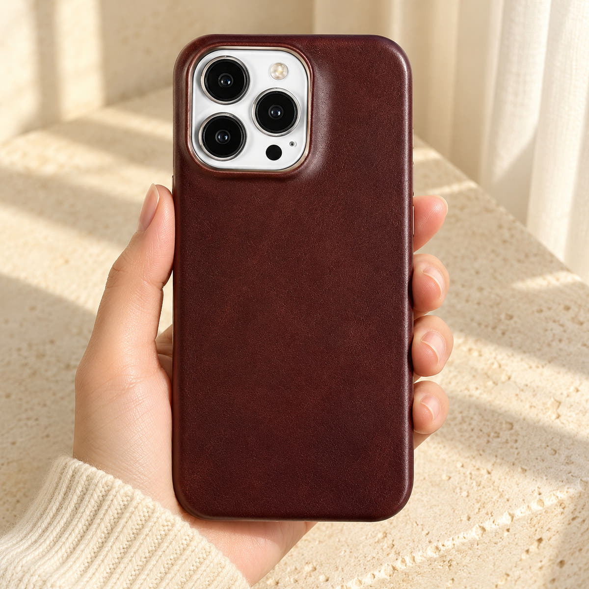 Minimal leather-look iPhone case in Burgundy, held upright against a cream background.