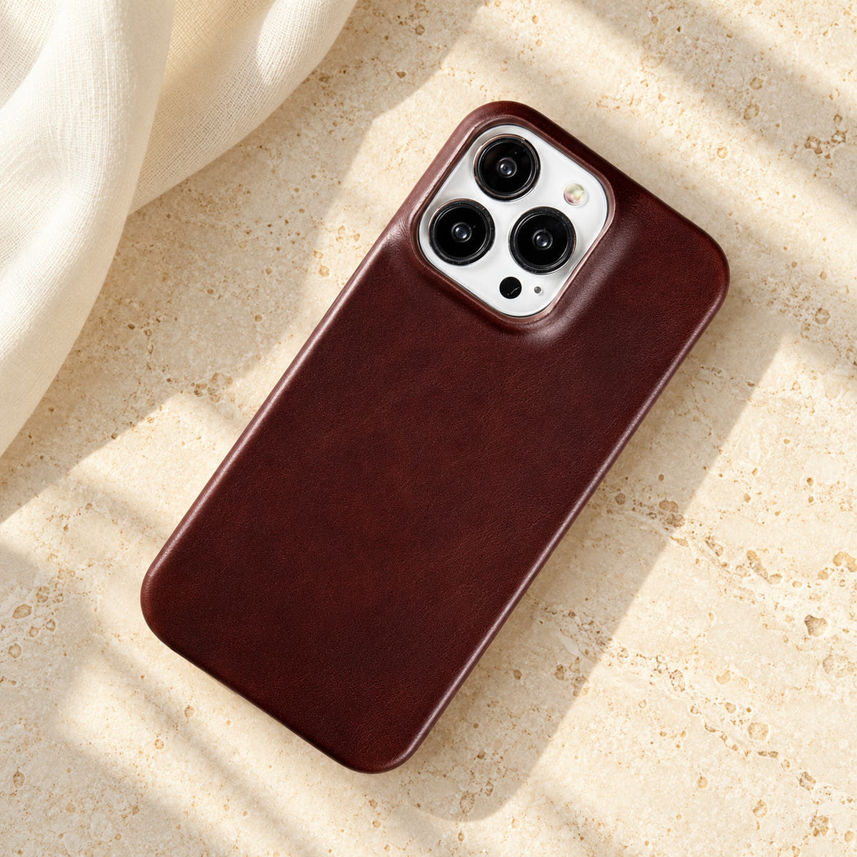 Minimal leather-look iPhone case in Burgundy, full rear view on an ivory tabletop.