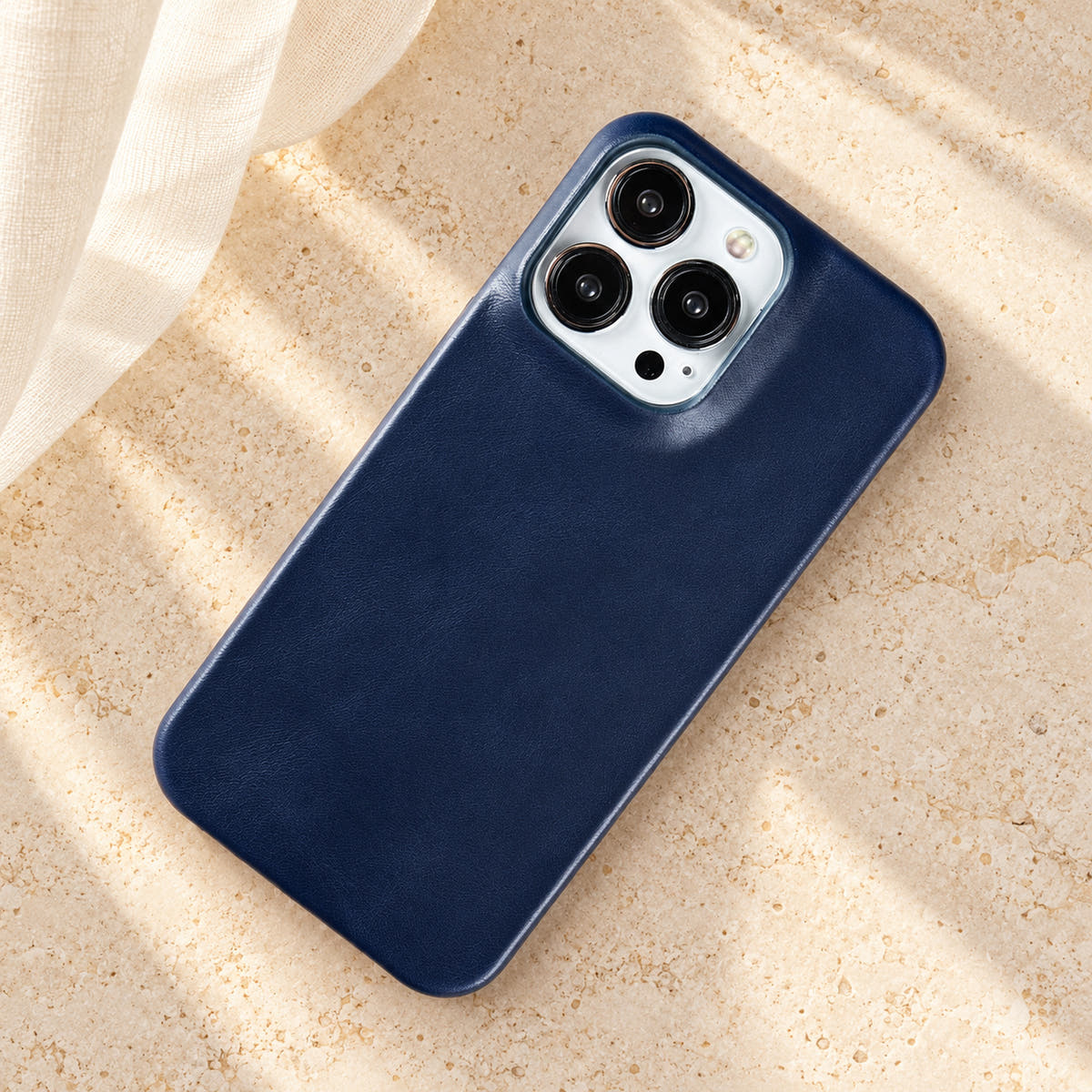 Minimal leather-look iPhone case in Midnight Blue, full rear view on an ivory tabletop.
