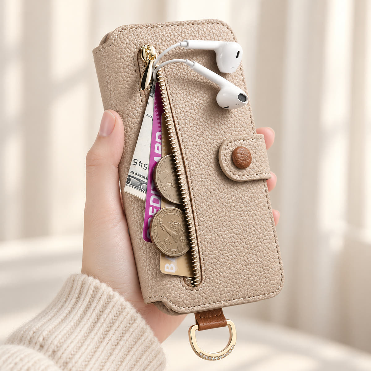 Beige iPhone wallet case with the front zip pocket open, showing illustrated cards, notes, coins and wired earphones beside the buttoned closure
