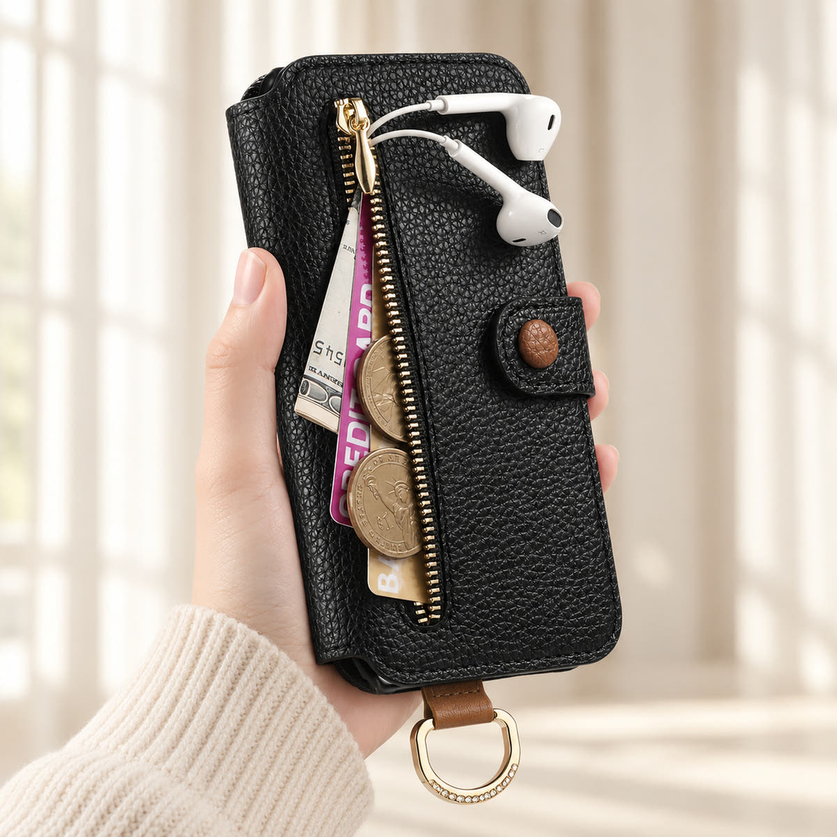 Black iPhone wallet case with the front zip pocket open, showing illustrated cards, notes, coins and wired earphones beside the buttoned closure